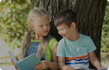 A young boy and girl sit against a tree while reading books