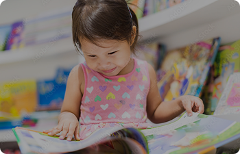 Small child reads from a book while smiling