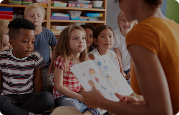 A teacher reads a book to a group of sitting children