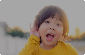 A young child holds her hand to her ear in a listening pose
