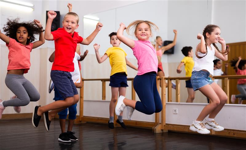 A group of children jump in the air while dancing in a studio