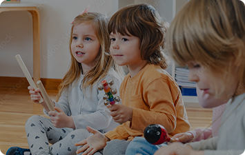 A group of children sit on the floor while playing with musical toys