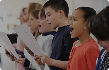 A group of children stand in a line while singing and holding sheet music.