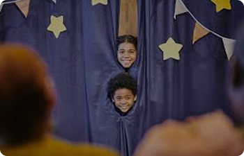 Two children peaking through a starry purple curtain