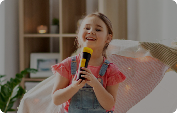A girl in overalls singing into a microphone on a couch